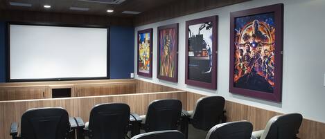 A movie theater with rows of seats, a large screen, and framed movie posters on the wall.