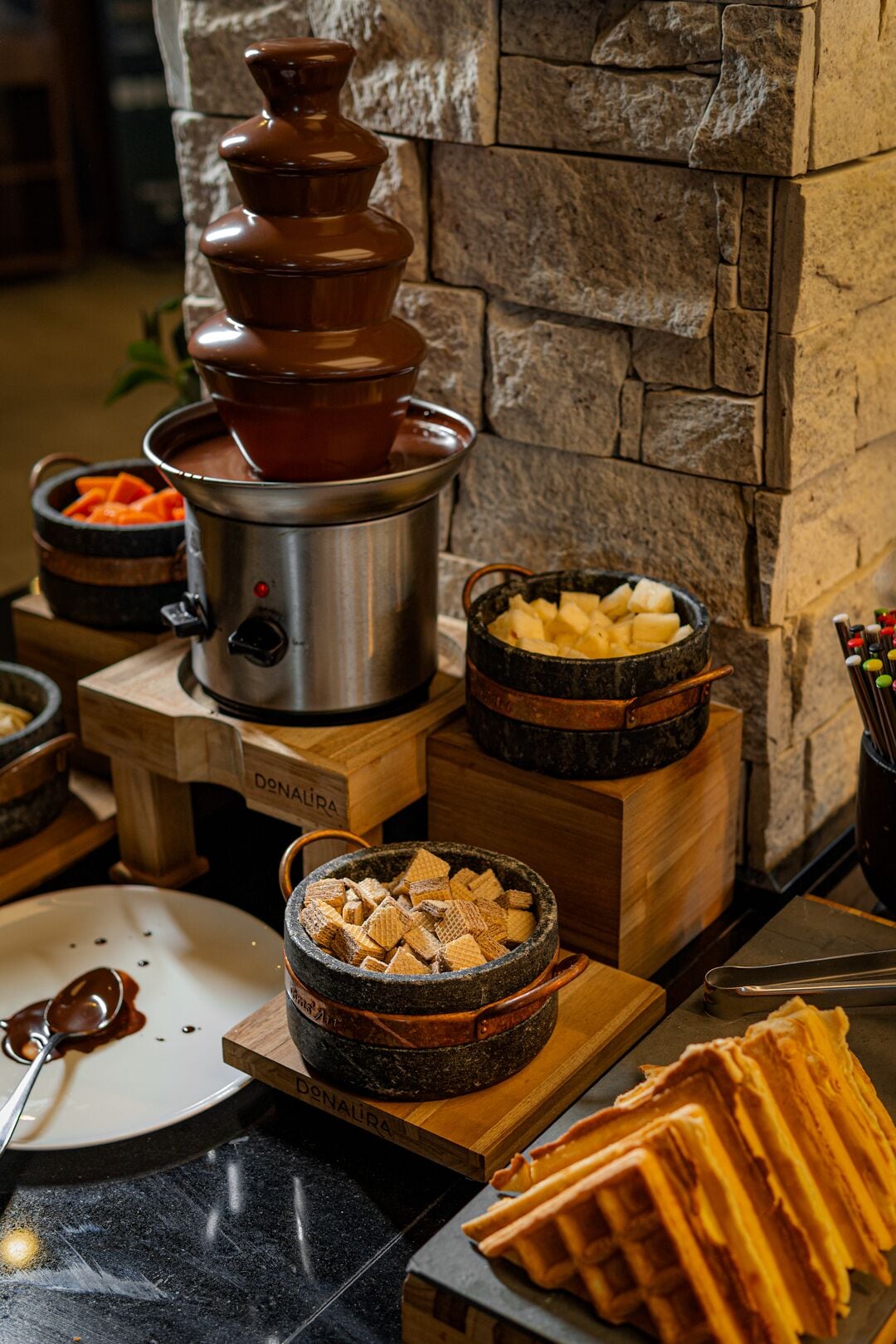 A buffet setup with a variety of food items including a hot pot, a bowl of sliced potatoes, and a plate with a waffle.