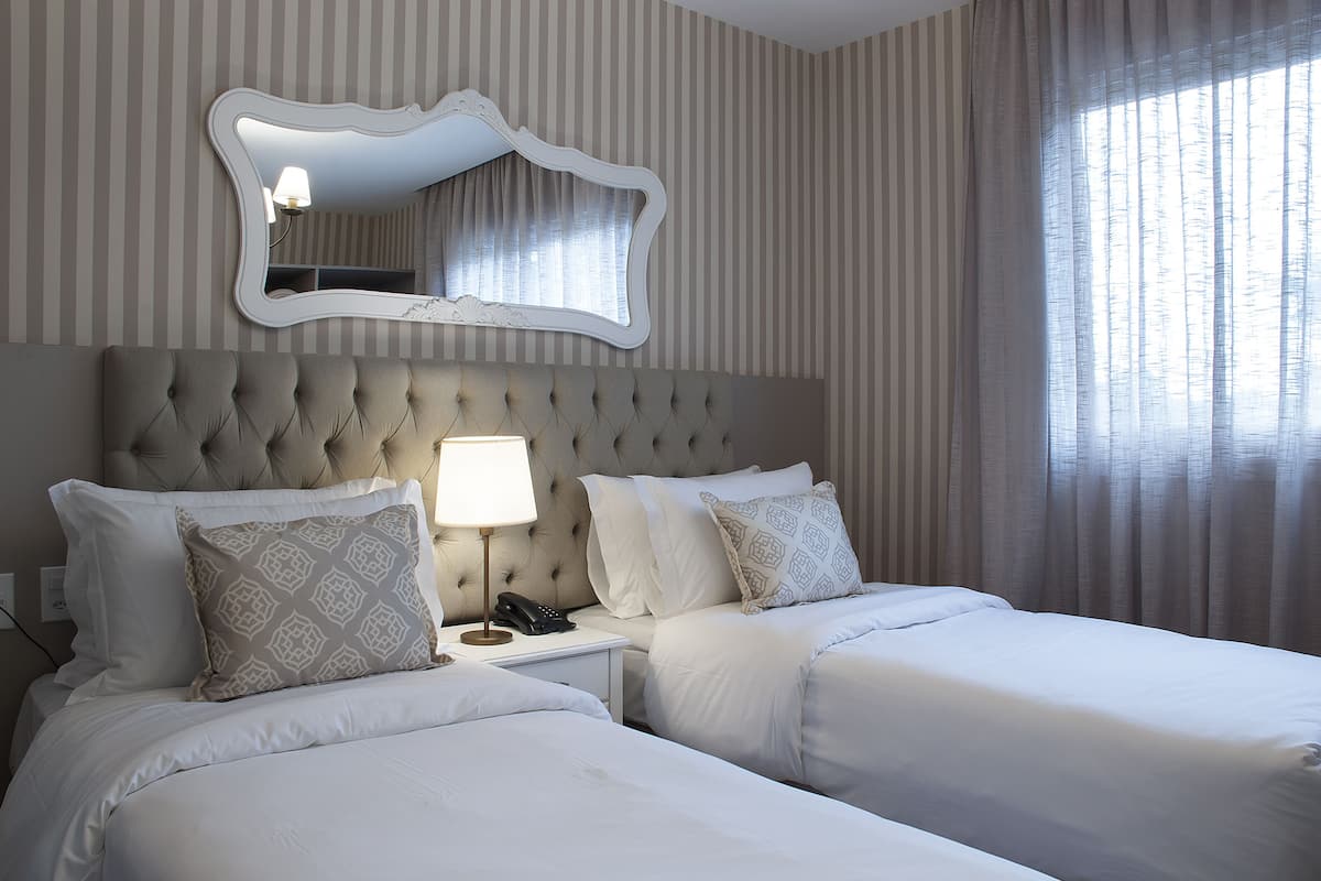 A hotel room with two beds, a large mirror, and a nightstand with a lamp and phone.