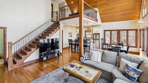 A spacious living area with a wooden staircase, a flat-screen TV, a sofa, and a dining area.