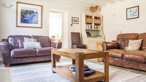 A living room with a brown leather sofa, a wooden coffee table, and a bookshelf. - 3 bedroom accommodation in Boscastle (Boscastle)