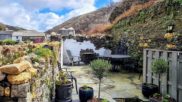 A stone-walled outdoor patio with a table and chairs, surrounded by potted plants and a small garden area. - 3 bedroom accommodation in Boscastle (Boscastle)