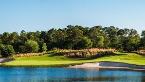 Un parcours de golf avec un plan d’eau au premier plan et une zone boisée en arrière-plan.