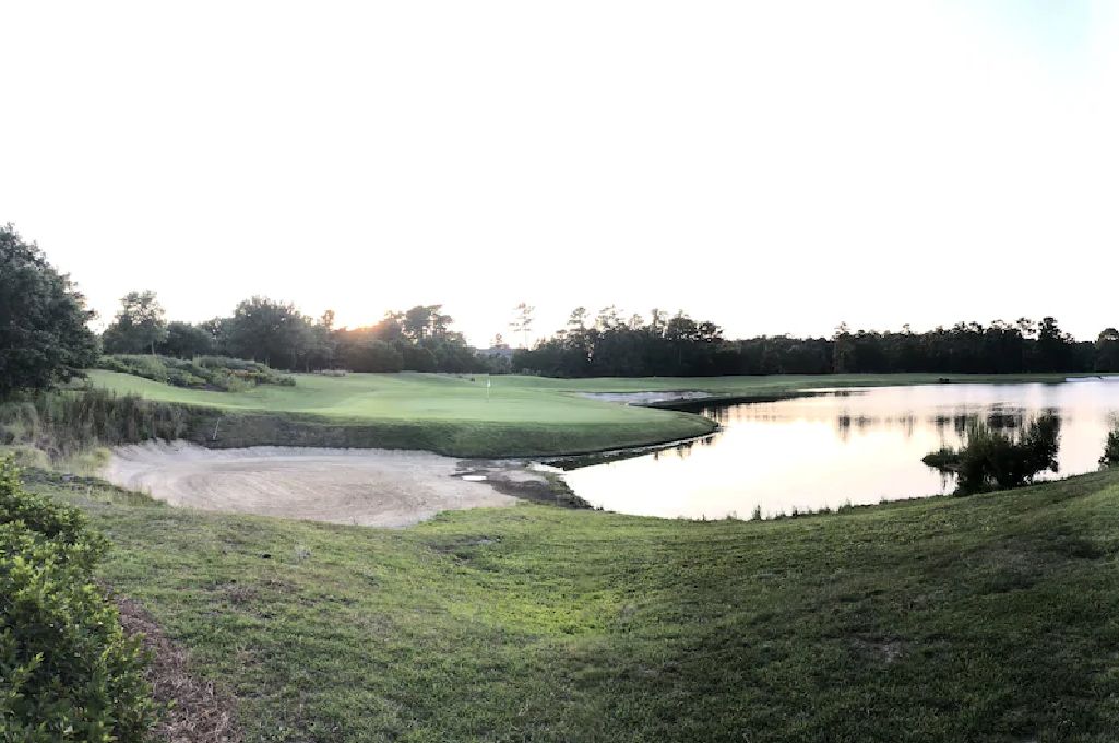 Un parcours de golf avec un étang, entouré d’arbres et de zones herbeuses.