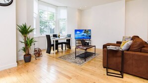 Una sala de estar moderna con un sofá marrón, una mesa de comedor con sillas, un televisor y un ventanal grande.