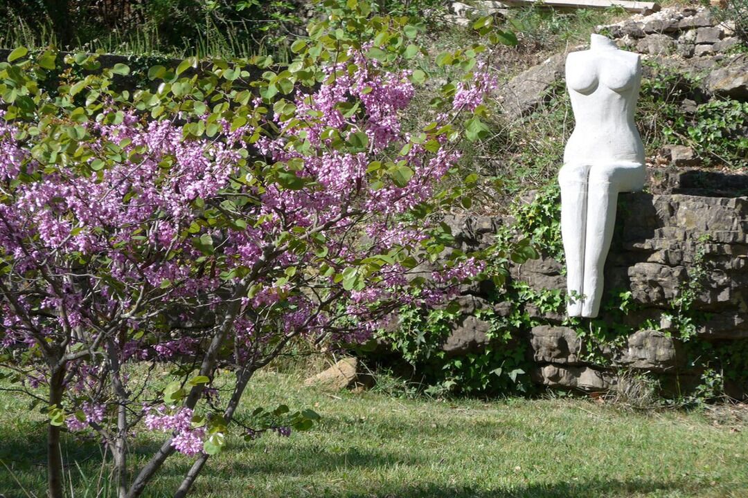 A garden with blooming purple flowers and a white sculpture against a stone wall.