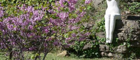 A garden with blooming purple flowers and a white sculpture against a stone wall.