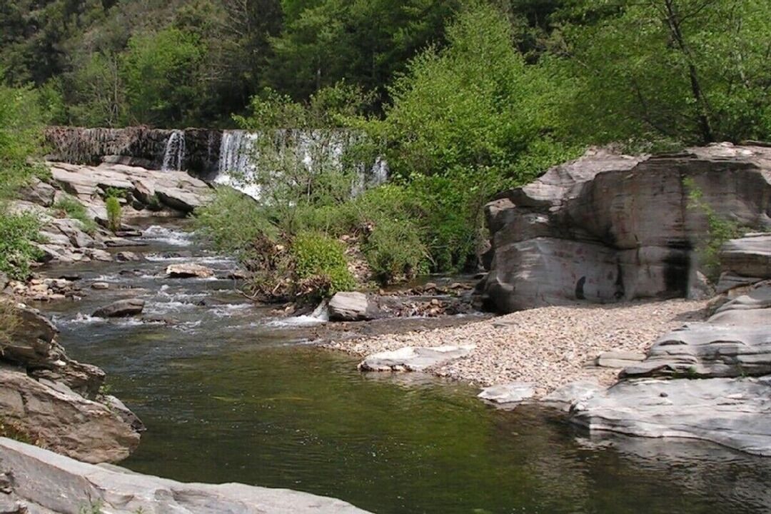 A natural landscape with a waterfall, rocky terrain, and dense greenery.