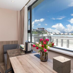 A hotel room with a large window, a table with a coffee maker, a vase of tulips, and a tissue box. - Atour Hotel (Lhasa)