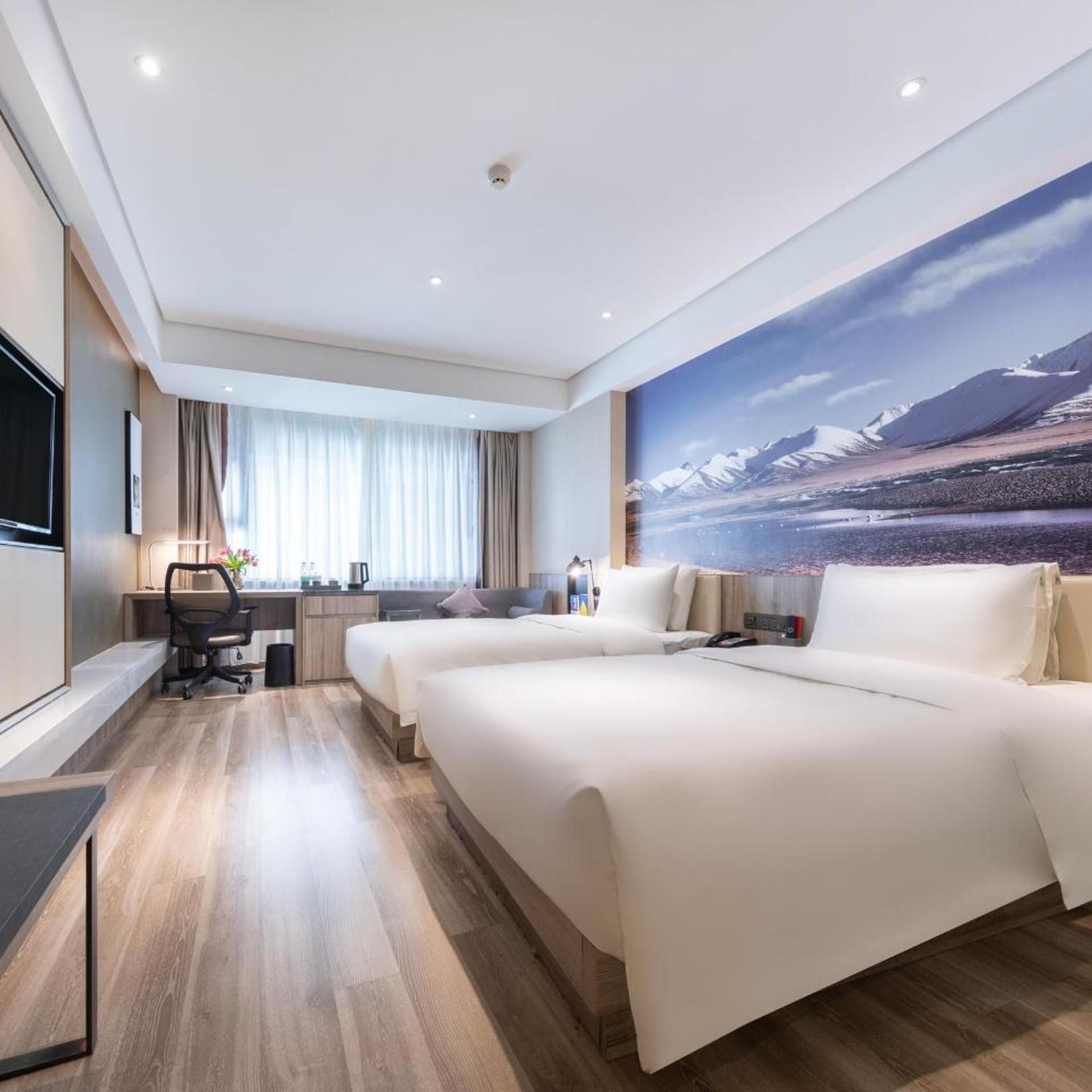 A hotel room with a large bed, a desk, a chair, a TV, and a scenic wall mural.
