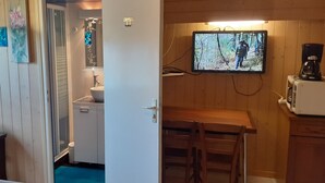 Un interior de madera con una zona de cocina, una mesa de comedor y un televisor que muestra una escena al aire libre.