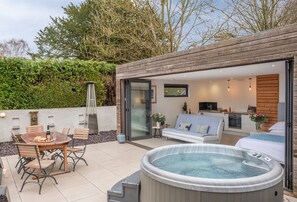 Ein moderner Außenbereich mit Whirlpool, Esstisch mit Stühlen und einer gemütlichen Sitzecke mit Sofa und Fernseher.