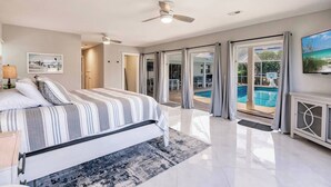 Een slaapkamer met een groot bed, een plafondventilator en uitzicht op een zwembad door glazen deuren.