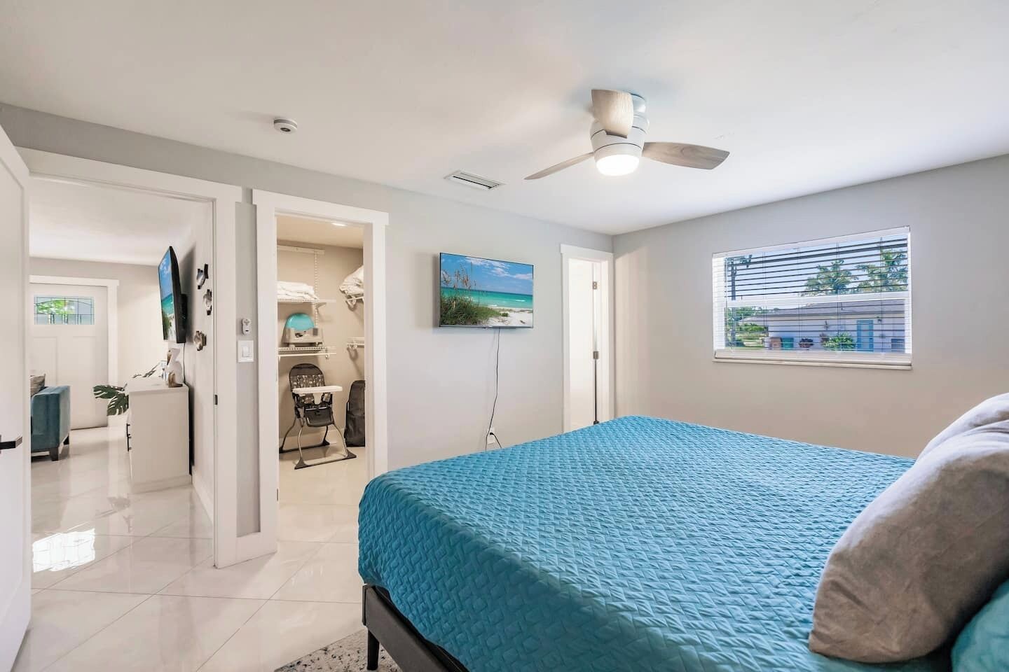 A bedroom with a bed, a ceiling fan, a window with blinds, and a door leading to a bathroom.