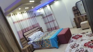 A bedroom with a bed, nightstand, wooden wardrobe, and a red ottoman. - Lovely 3-bed Pyramids Viewapartment in Kafr Nassar (Giza)