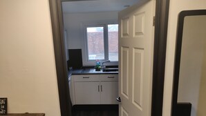 A narrow hallway leading to a kitchen with white cabinets, a window, and a door. - Riverside Park Penthouse Apartment in St Neots (Eaton Ford)