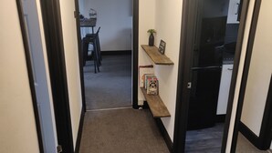 A narrow hallway with a carpeted floor, a wooden bench, a small shelf with books, and a 'Welcome' sign. - Riverside Park Penthouse Apartment in St Neots (Eaton Ford)