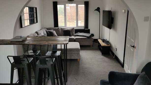A compact living space with a dining area, a sofa, and a TV mounted on the wall. - Riverside Park Penthouse Apartment in St Neots (Eaton Ford)