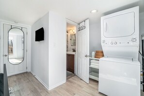 Un lavadero con lavadora, un espejo y una puerta que da al baño.