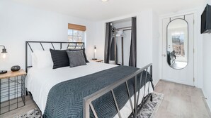 Un dormitorio moderno con una cama, mesitas de noche, un espejo y vistas al exterior.