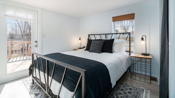 Un dormitorio con cama, mesitas de noche, ventana y vistas al exterior.