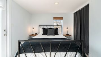 A bedroom with a bed, bedside tables, a window with blinds, and a door.