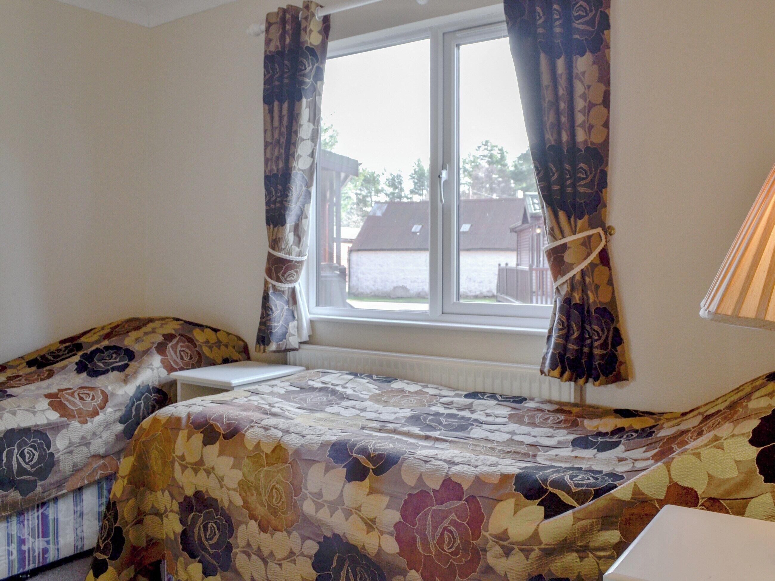 A room with two beds, a window with curtains, a radiator, and a lamp.