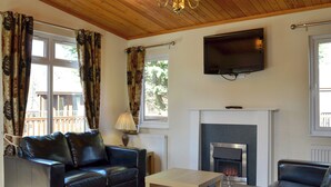 A living room with a fireplace, a sofa, a coffee table, and a TV mounted on the wall. - 2 bedroom accommodation in Dinnet, near Ballater (Dinnet, near Ballater)