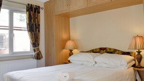 A neatly made bed with white linens and a rolled towel, two bedside lamps, and a window with curtains. - 2 bedroom accommodation in Dinnet, near Ballater (Dinnet, near Ballater)