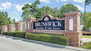 Een bord voor Brunswick Plantation & Golf Resort, met een bakstenen muur en groen op de achtergrond.
