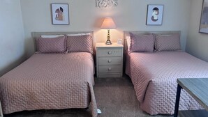 Een slaapkamer met twee bedden, een nachtkastje met een lamp en een bord aan de muur.