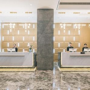 Zona de recepción de hotel con suelo de mármol, dos mostradores y luminarias modernas.