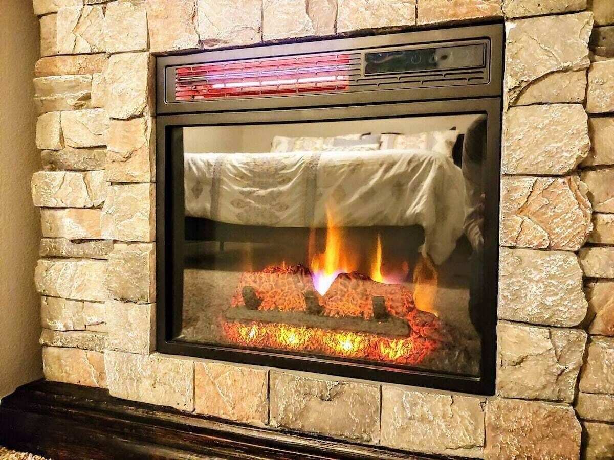 Ein Kamin aus Stein mit Glastür, in dem ein Feuer brennt, und ein Bedienfeld darüber.