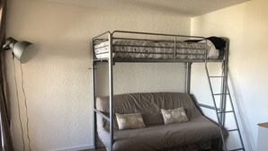 Een stapelbed met een ladder, een bank en een lamp in een kamer met houten vloeren en een gestructureerde muur.