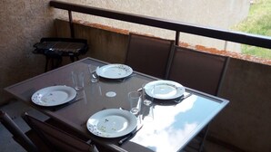 Een eettafel gedekt voor vier personen, met stoelen, een kleine grill en uitzicht op de natuur.