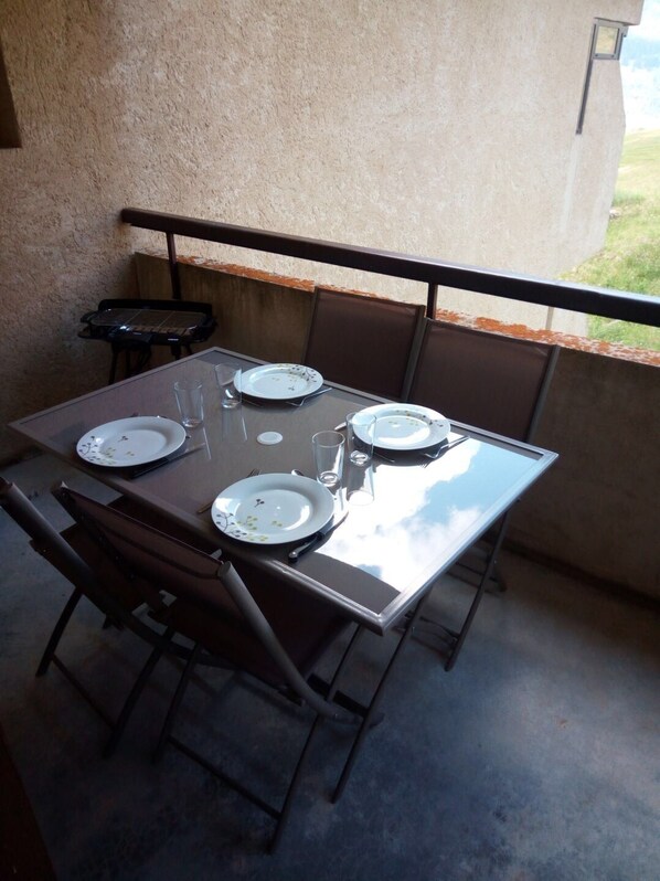 A dining table set for four with chairs, a small grill, and a view of the outdoors. - Charming Winter/Summer Studio at Queyras Park (Molines-en-Queyras)