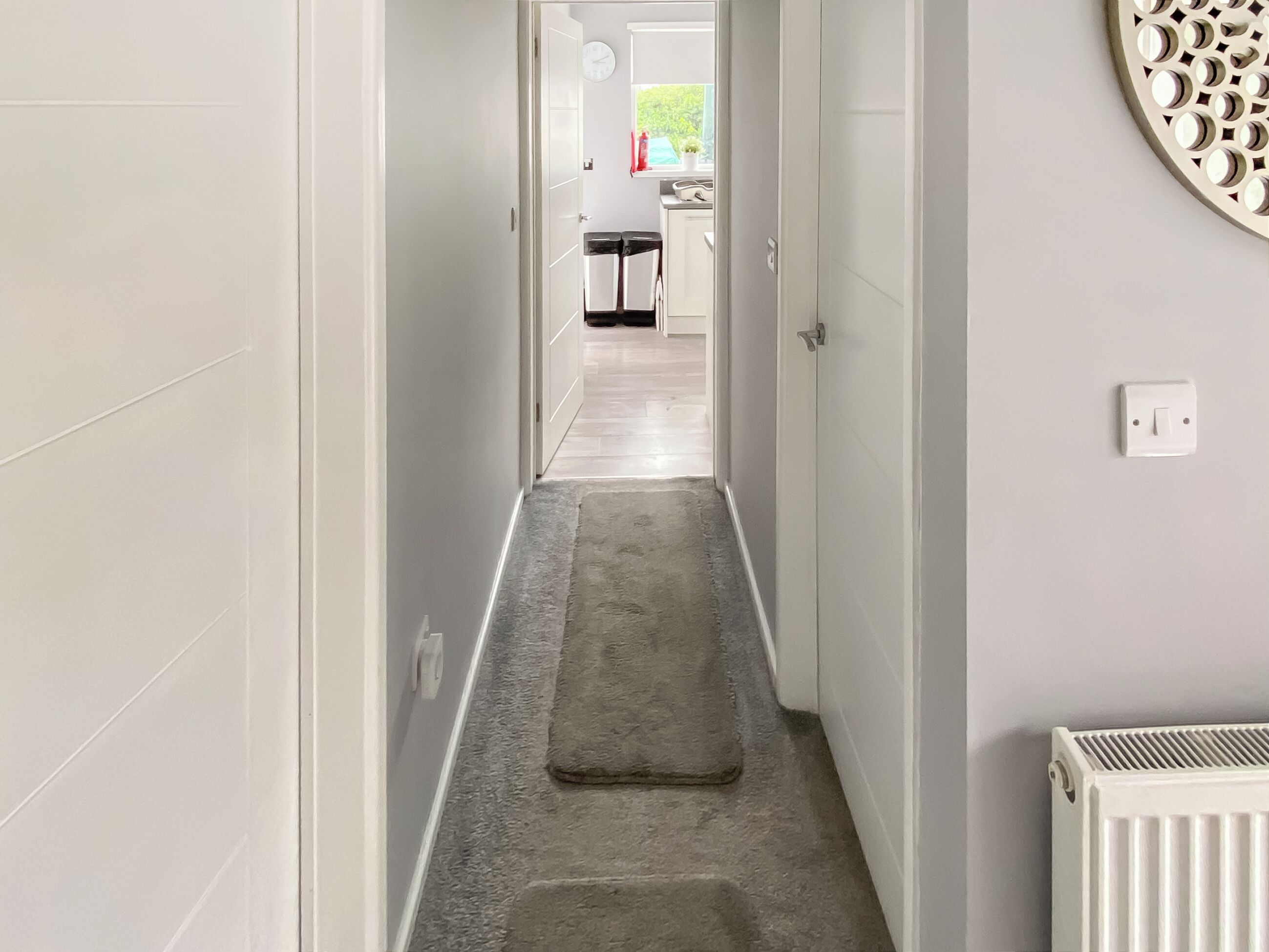 A narrow hallway with a rug, a radiator, and a door leading to a kitchen area.