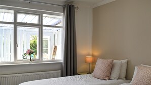 Een hotelkamer met twee bedden, een raam met gordijnen, een radiator en een lamp op een nachtkastje.