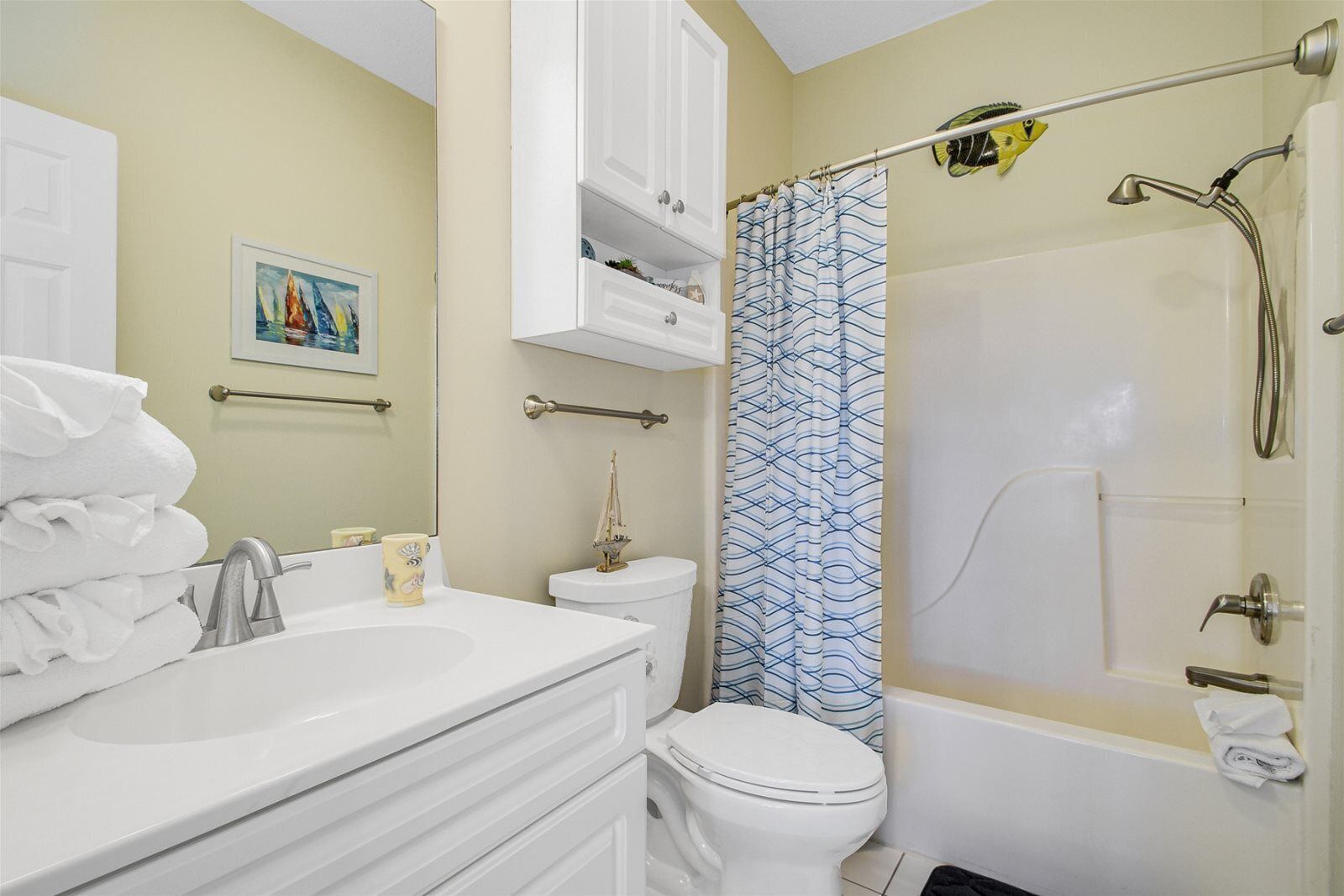 A bathroom with a white sink, toilet, and bathtub. There is a towel rack with towels and a painting on the wall.