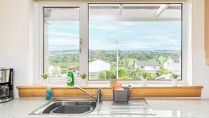 A kitchen with a sink, a coffee maker, and a window with a view of houses and greenery. - 3 bedroom accommodation in Dunblane (Dunblane)