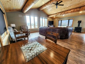 A spacious living room with a wooden ceiling, a large chessboard on a wooden table, and a cozy seating area with a fireplace. - Large Home in Crested Butte | 5 Bedroom | Game Room | Rainbow Park | Mt CB View (Crested Butte)