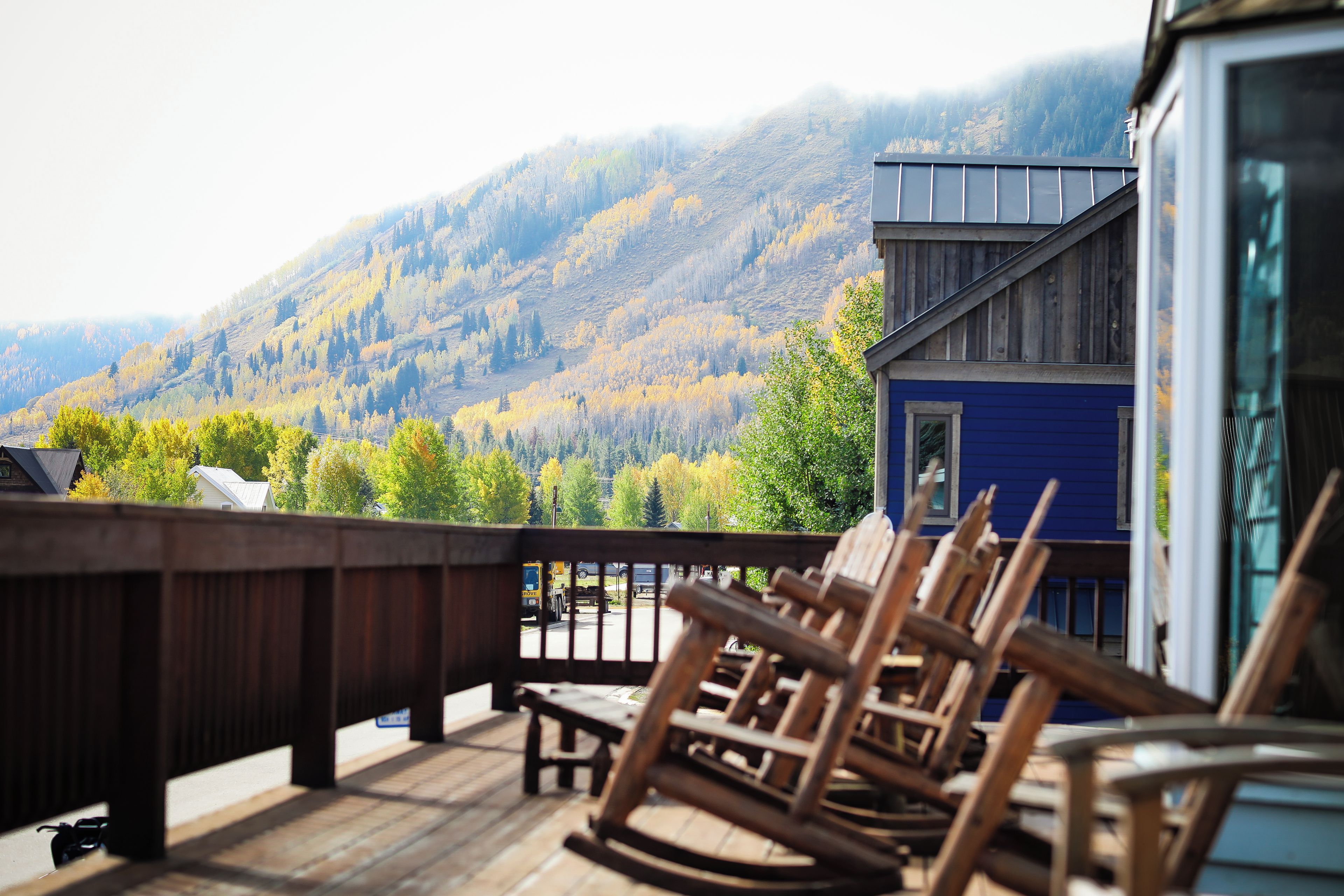 A wooden deck with chairs and a table, overlooking a mountainous landscape with autumn foliage.