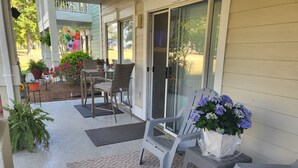 A covered porch with outdoor furniture, potted plants, and a sliding glass door leading to a garden.