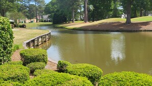 A serene park with a pond, neatly trimmed bushes, and a wooden bridge.