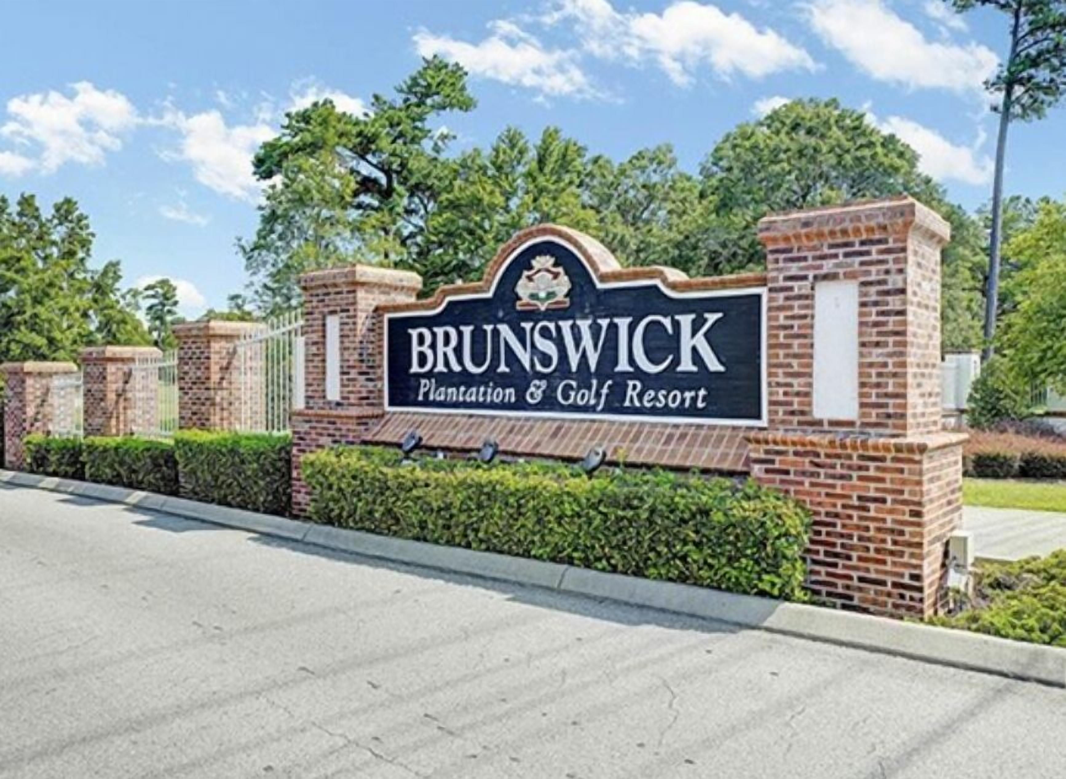 Een bord voor Brunswick Plantation & Golf Resort, met een bakstenen muur en begroeiing op de achtergrond.