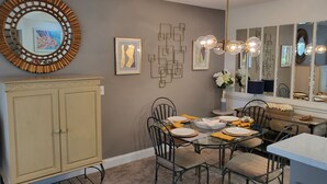 A dining area with a round mirror, framed artwork, a chandelier, and a dining table set for four.