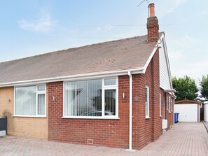 Une maison en briques rouges, avec un toit en tuiles, de grandes fenêtres et une cheminée.