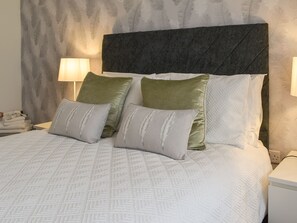 Un lit avec une couvre-lit à motifs, deux oreillers ornés de motifs de feuilles, une tête de lit sombre et deux lampes de chevet.