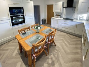 Une cuisine moderne avec des meubles blancs, une table à manger avec des sets de table et un parquet disposé en motif chevrons.