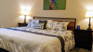 A neatly made bed with a patterned bedspread and pillows, flanked by two bedside tables with lamps, in a room with a single wall-mounted picture of a bird. - Hillside Hideout - Great for groups! - Great Views (Branson)
